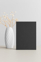Black invitation card mockup with a gypsophila on the beige table. 5x7 ratio, similar to A6, A5.