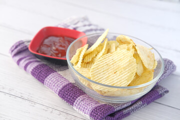 Bowl with tasty potato chips on wooden background .