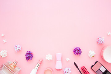 Various decorative makeup cosmetics and fresh cherry blossoms on light pink table background. Pastel color. Different beauty essentials for women. Empty place for text or logo. Top down view. Closeup.