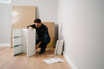 Portrait of man assembling furniture. Do it yourself furniture assembly. - 413224990