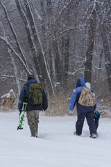 Two men with backpacks and fishing gear go fishing in winter. Drifts and snowfall, frost on tree branches