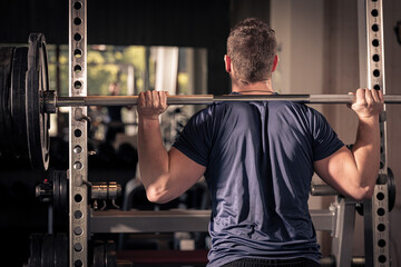 male athlete is lifting a barbell in a fitness center, backview