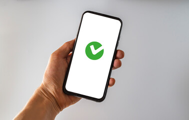 Holding a smartphone with a green checkmark to indicate an approved, approved, completed, or...