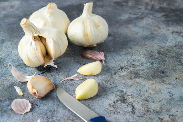 Heads and cloves of garlic (Allium sativum) peeled and crude on a bluish-grey stone with a small knife. Spicy cooking ingredient. Healthy food with vitamins. Vegetables and vegetarians.