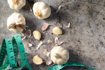 Peeled garlic (Allium sativum) heads and cloves on a grey stone next to a tape measure. Concept of healthy food with vitamins. Vegetables and vegetarians.