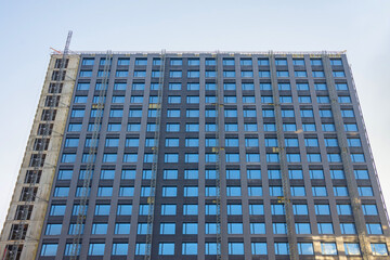 Facade cladding of a multi-storey building, many windows, and a construction elevator.