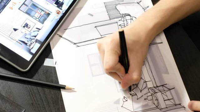 The hand of an architect drawing a perspective of the bedroom with a black pen. On a black wooden desk where a tablet and pencil are placed. timelapse