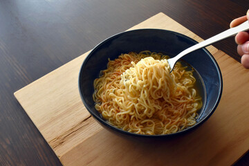 Instant noodles on fork on a dark blue bowl. Copy space is on the left side.