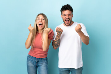 Young caucasian couple isolated on blue background celebrating a victory
