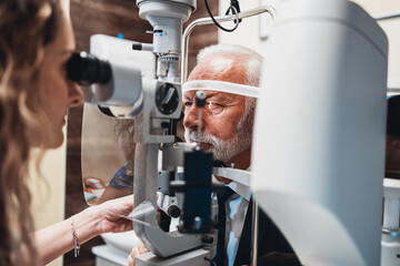 Elegant senior bearded man receiving ophthalmology treatment. Doctor ophthalmologist checking his eyesight with modern equipment. - obrazy, fototapety, plakaty