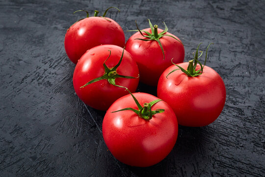 Ripe red tomatoes on a dark stone background. Culinary image of fresh tomatoes ready to cook.