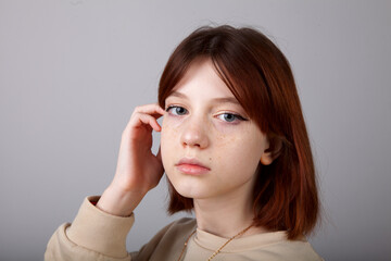 Portrait of an eleven-year-old red-haired teenage girl with freckles. Photo in the studio. Teenage makeup.