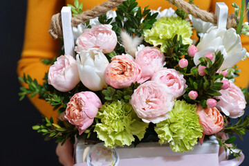 a young girl in a mustard dress holds in her hands a beautiful composition of flowers in a box created by a florist. the concept of a pleasant sale for a holiday. close-up