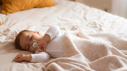 Cute Baby  sleeping in bed, covered with a beige blanket 
