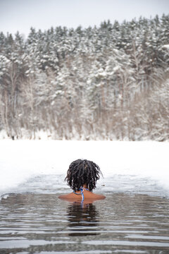 Beautiful girl swimming in the cold water of a lake or river, cold therapy, ice swim with winter landscape and forest on background, vertical