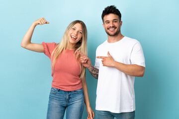Young caucasian couple isolated on blue background making strong gesture