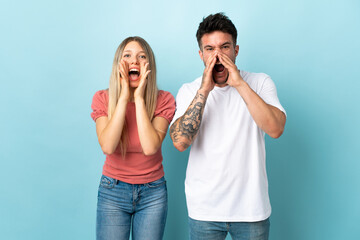 Young caucasian couple isolated on blue background shouting with mouth wide open