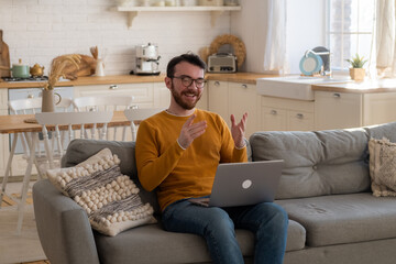 Side view handsome young businessman in eyewear working with computer remotely, having chat with friends or collegs. Pleasant happy man communicating in social network
