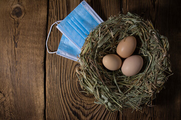eggs in a nest of straw with a medical mask on vintage wood background with copy space, easter quarantine concept.