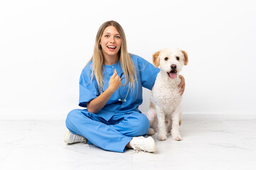 Young veterinarian woman with dog sitting on the floor with surprise facial expression