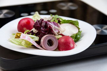 some salad and a pink centimeter on white plate standing on black scales on white background
