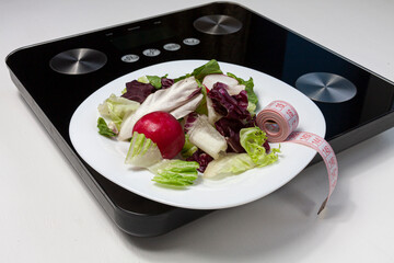 some salad and a pink centimeter on white plate standing on black scales on white background