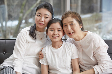 Fototapeta premium Little kid daughter and old mother while sitting on sofa at home