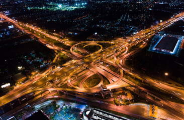 Fototapeta na wymiar Car traffic transport on multiple lane highway or winding road expressway in Asia city at night, drone aerial view, high angle. Civil engineering technology, Asian transportation concept