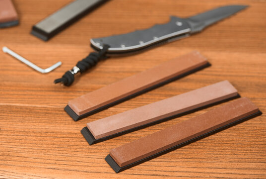 Various whetstones, a folding knife and a hex l-key on wooden background
