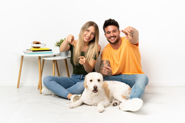 Young caucasian couple with dog staying at home points finger at you with a confident expression