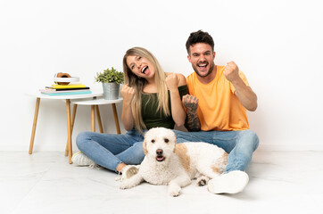 Young caucasian couple with dog staying at home celebrating a victory in winner position