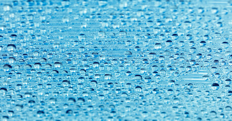 Water drops on blue glass as an abstract background.