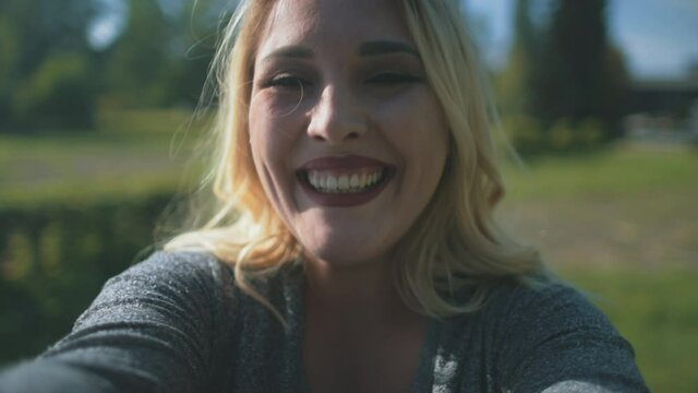 Woman show tongue, wink eye at park closeup. Body positive girl have fun at sun trees. Nature landscape at autumn sunny day. Happiness, joyful holiday. Happy and funny blondy lady. Cinematic portrait
