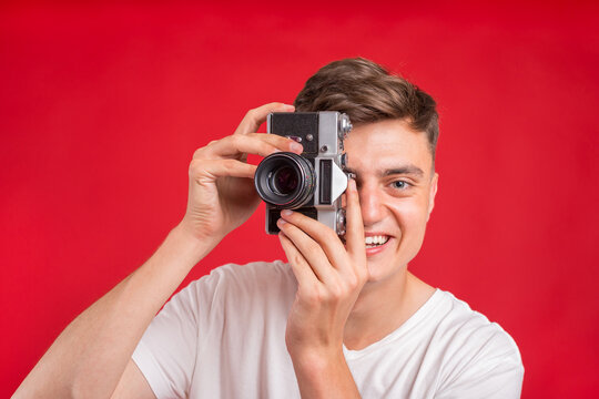 Say cheese! Young man take photo with retro dslr camera looking at camera over gray abackground. Portrait of positive man in hat with retro camera standing isolated