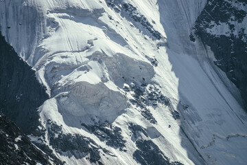 Nature background of big rocky snowy mountain wall with white glacier and snow cornice close up....