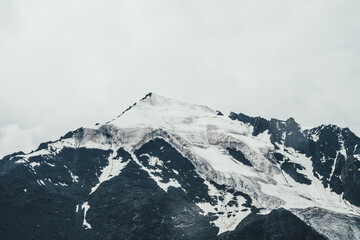 Obraz premium Minimalist monochrome atmospheric mountains landscape with big snowy mountain top in overcast rainy weather. Awesome minimal scenery with glacier on rocks. Black white high mountain pinnacle with snow