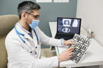Doctor wearing a protective face mask analyzes results of a patient's lungs CT scan at a medical clinic. Diagnosis of pneumonia, CT of lungs, coronavirus