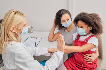 African American child with her mother wearing protective face masks at the general practitioner consultation. Global pandemic