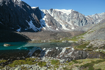 Snowy mountain reflected in clear water of glacial lake. Beautiful sunny landscape with glacier reflection in water surface of mountain lake under clear sky. Snow on rock reflected in mountain lake.