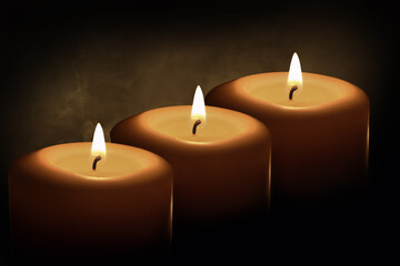 Three large candles burn in the dark. Close-up
