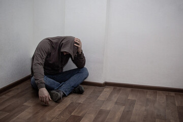 desperate young drug addict wearing hood and sitting alone in corner