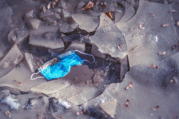 face mask pollution, Discarded coronavirus single-use face masks in winter, Environmental cities and nature plastic pollution. consequences of anti-epidemiological actions, blue mask in mud and ice