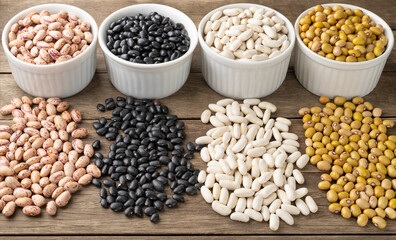 Closeup of assorted beans on white bowls over wooden table