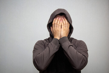 portrait of young adult man in the gray hood covered his face with his hands - obrazy, fototapety, plakaty