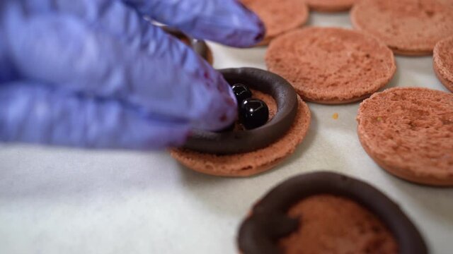 Close up view of many rows of brown open halves of macarons macaroon on a table. The cook stuffs them with currant berries.