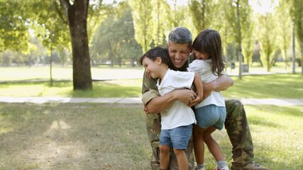 Happy family meeting father from military mission trip. Children running to man in uniform, dad hugging and cuddling kids outdoors. Family reunion concept