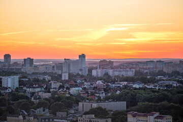 Panorama of a big city from a great height at sunset. View of the city of Minsk. Colorful red sky, many different houses and green trees on the streets of the city.