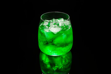 Glass with green cocktail with ice on black reflective surface