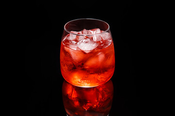 Glass with red cocktail with ice on black reflective surface