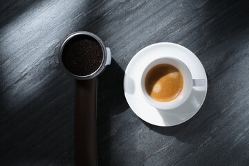 White cup with coffee on a black textured stone table, flat lay. Classic Italian breakfast. Italian coffee. Morning coffee in the sun, top view.